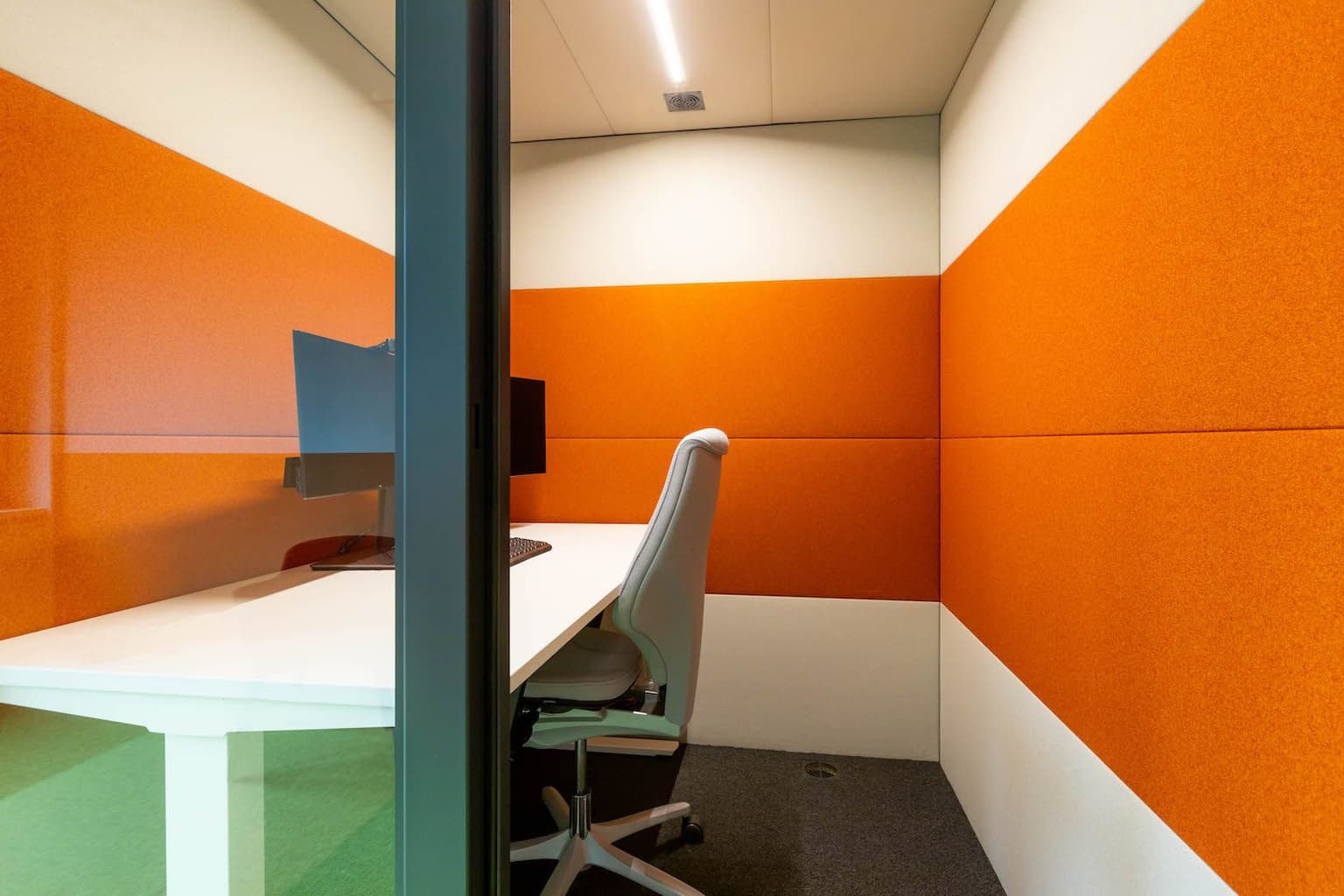 Binnenkant van een akoestische werkplek met wit bureau, witte bureaustoel en zwarte monitor erop. 