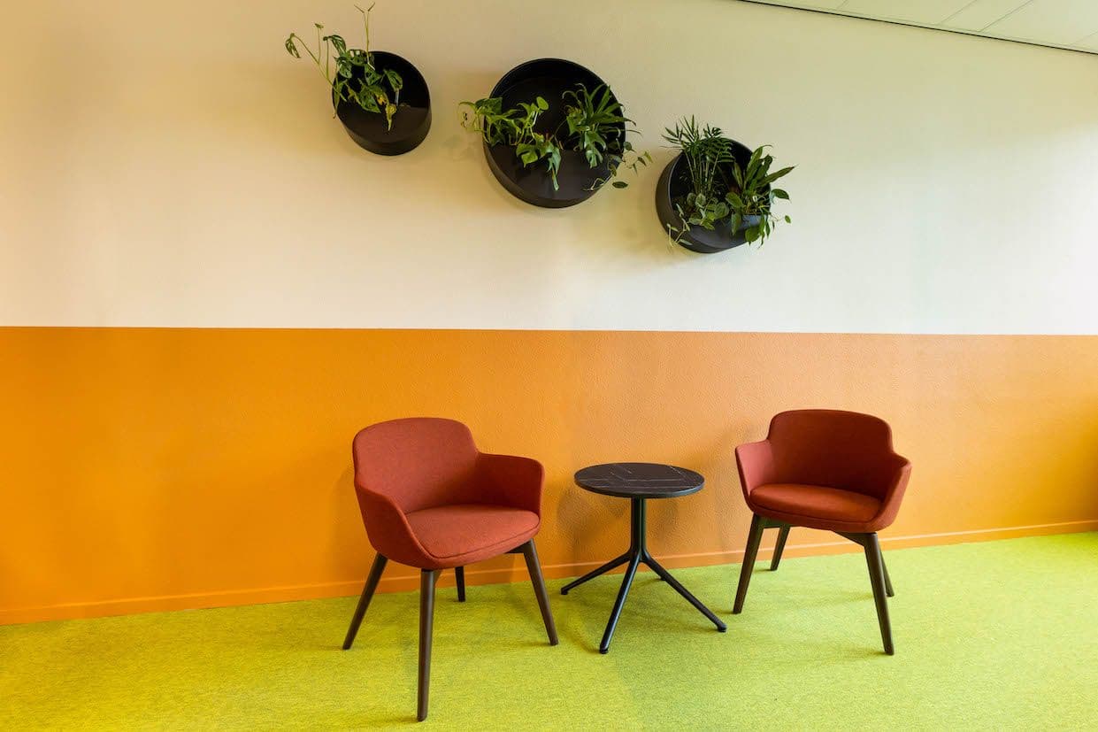 Zithoek in een kantoor met twee oranje stoelen en een zwarte koffietafel. 