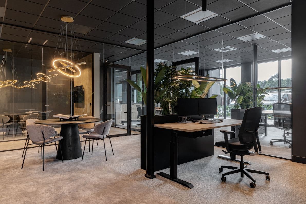 Werkplekken met zit sta bureaus en zwarte bureaustoelen erachter. 