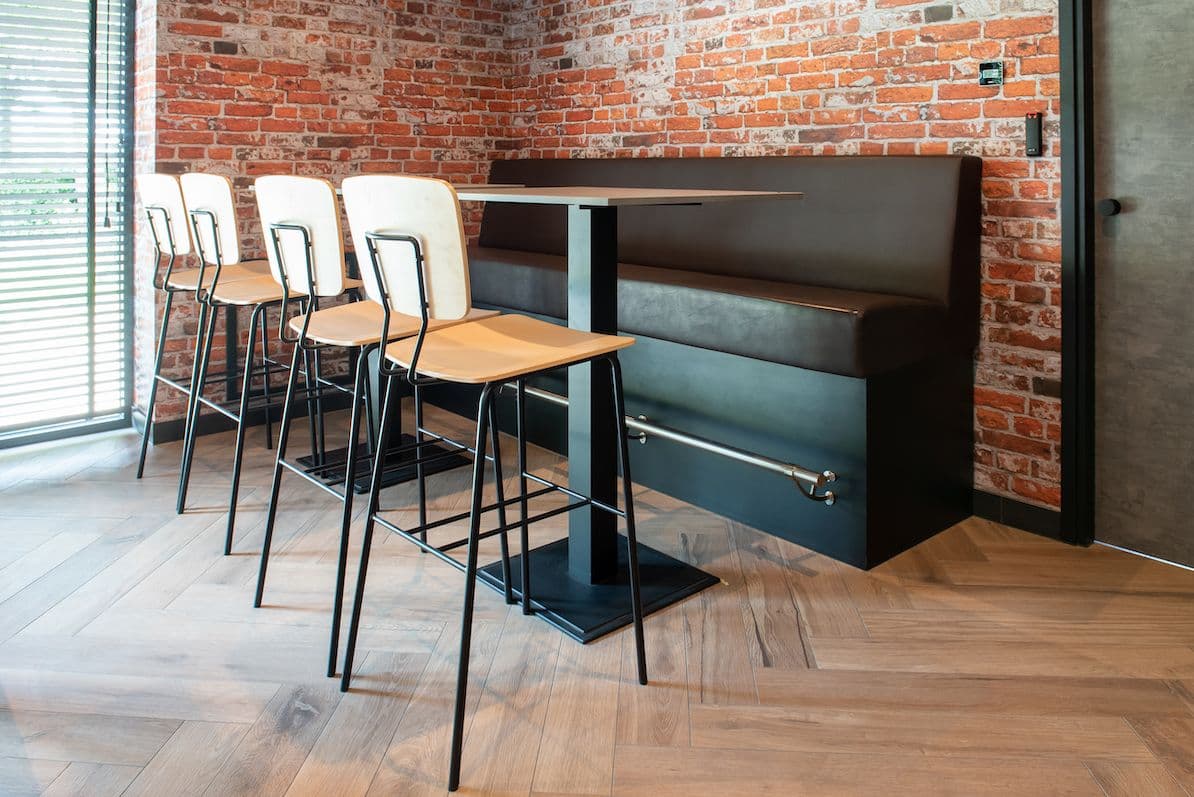 Hoge kantinetafel met vier houten barkrukken en een leren treinbank eromheen. 