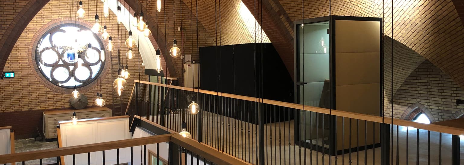 We zien de binnenkant van een kerkgebouw. Links in de hoek is een rozet en op de gallerij staat een akoestische telefooncel met een lichtgroene bekleding. Inzetbaar als akoestische kantoorunit en ter vervanging van systeemwanden kantoor. 