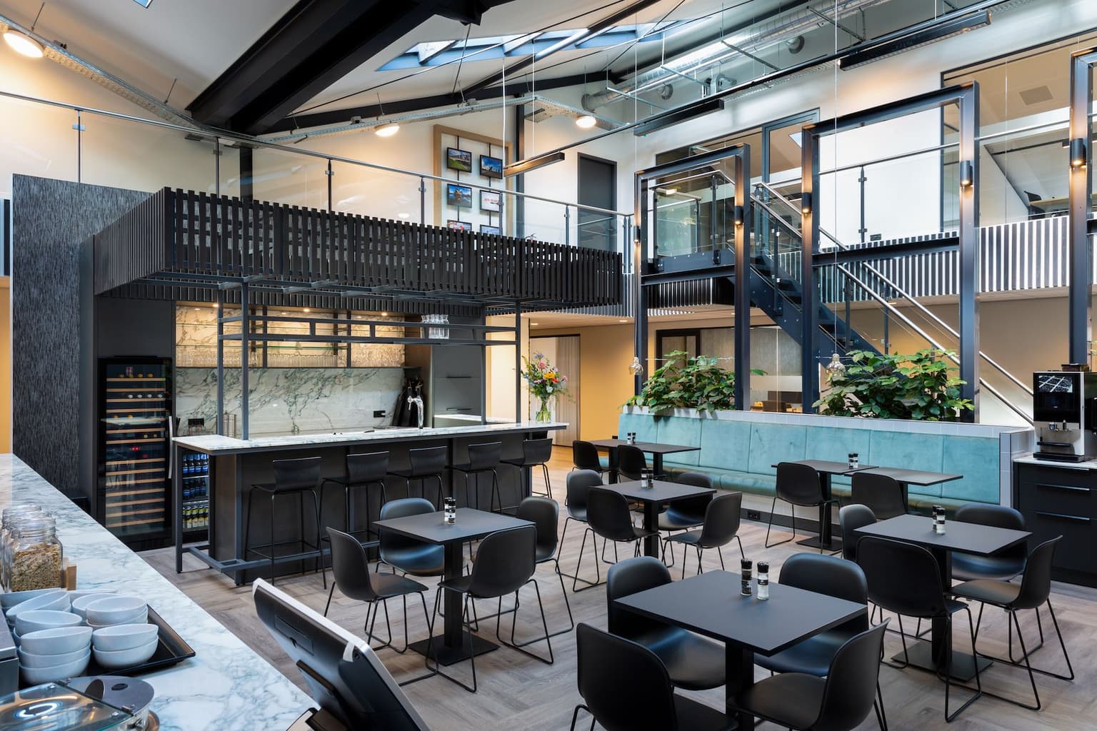 Kantine met daarin een zwarte bar, met een marmeren muur. In de kantine staan meerdere zitjes, met een zwarte tafel en vier zwarte stoelen eromheen. 