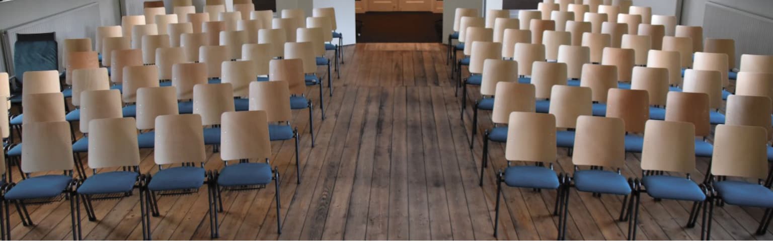 Kerkstoelen op een rij met een gangpad ertussen. Alle stoelen hebben een lichtblauwe zitting. 