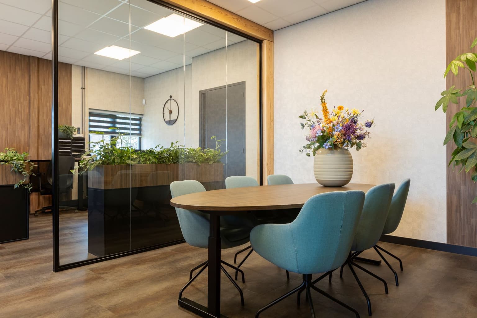 Vergaderruimte met blauwe stoelen en ovale vergadertafel. 
