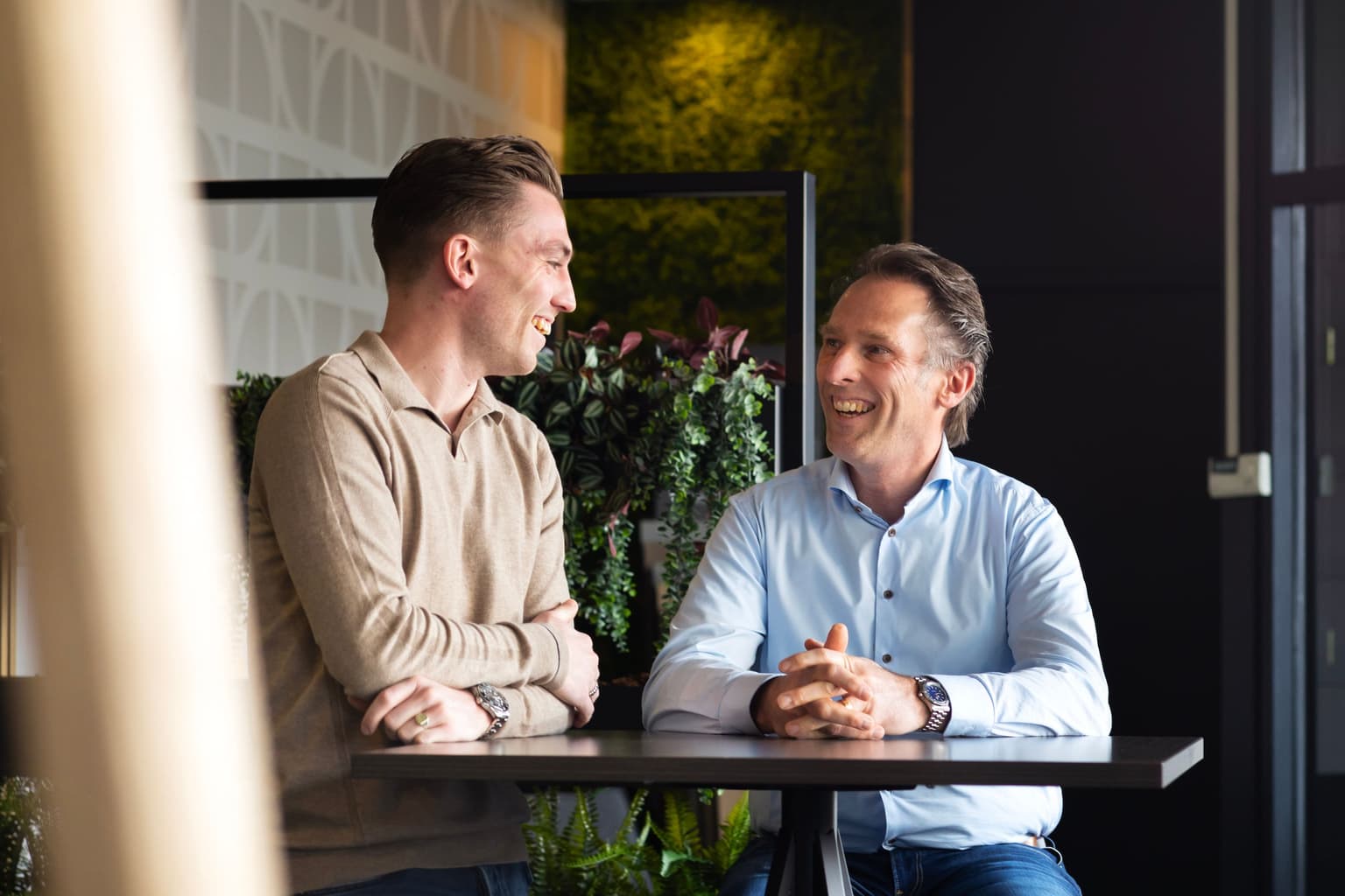 Joan en Casper van Blijderveen samen op de foto. Links staat Joan, die kijkt naar Casper en rechts zit Casper op een barkruk. 