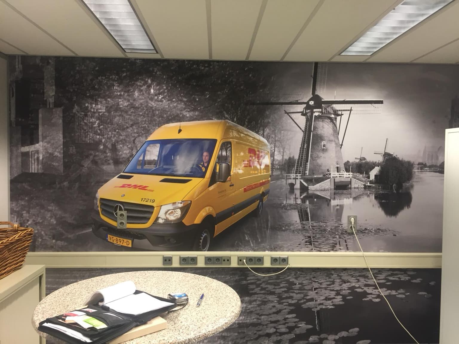 Visual op de muur met daarop een DHL-bus voor een oud-Nederlands landschap met een molen.