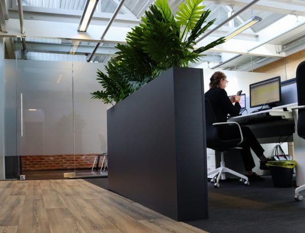 In het midden van het kantoor staat een plantenbak met groene kunstplanten erin.
