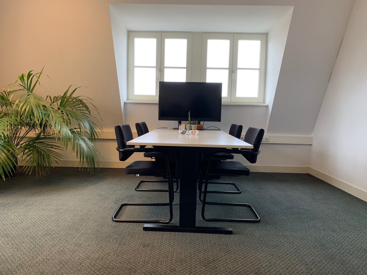 Vergadertafel met daaromheen vier zwarte vergaderstoelen met een u-poot. Aan de kop z'n kant staat een beeldscherm.