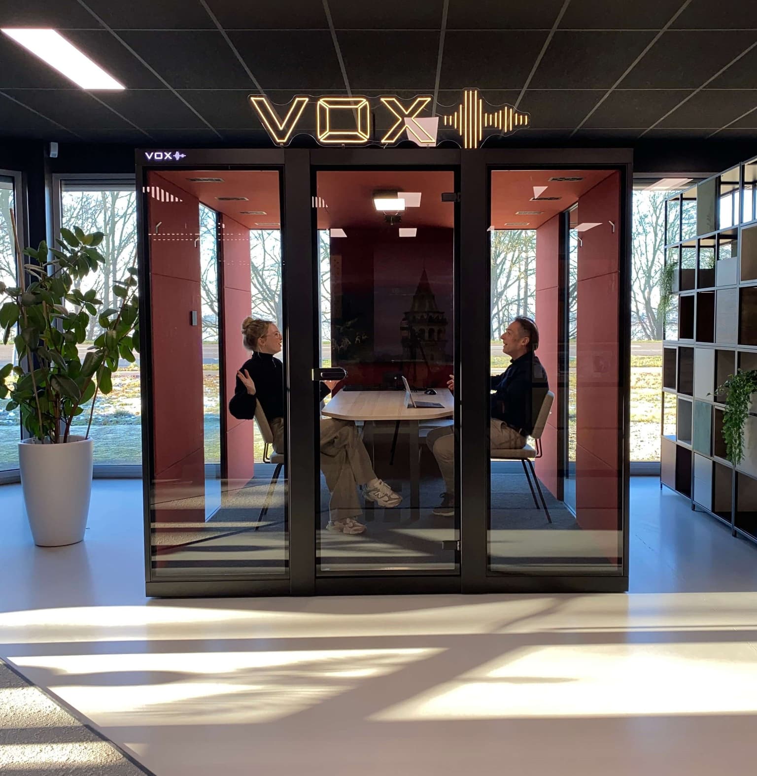 Zwarte vergadercabine met rode binnenkant in een showroom. 