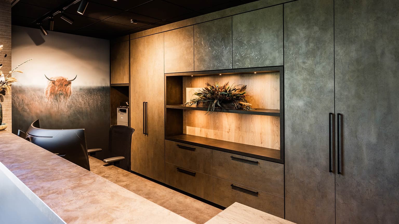 Receptiebalie met daarin een maatwerk achterkast. Hierin zit een open vak dat is verlicht. Links zien we een buffel op de muur.