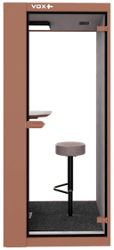 Akoestische telefooncel met een rozebruine buitenkant, een tafeltje in de belcel en een kruk erbij.