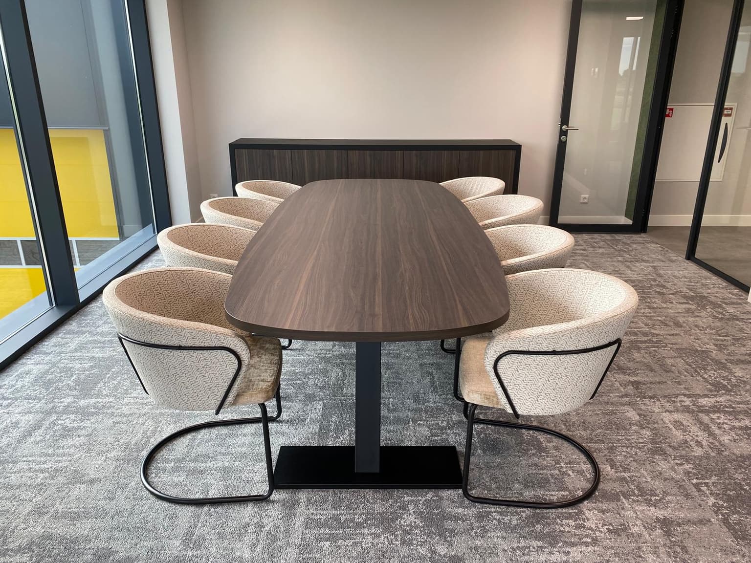 Donkerbruine vergadertafel met acht zandkleurige stoelen eromheen.