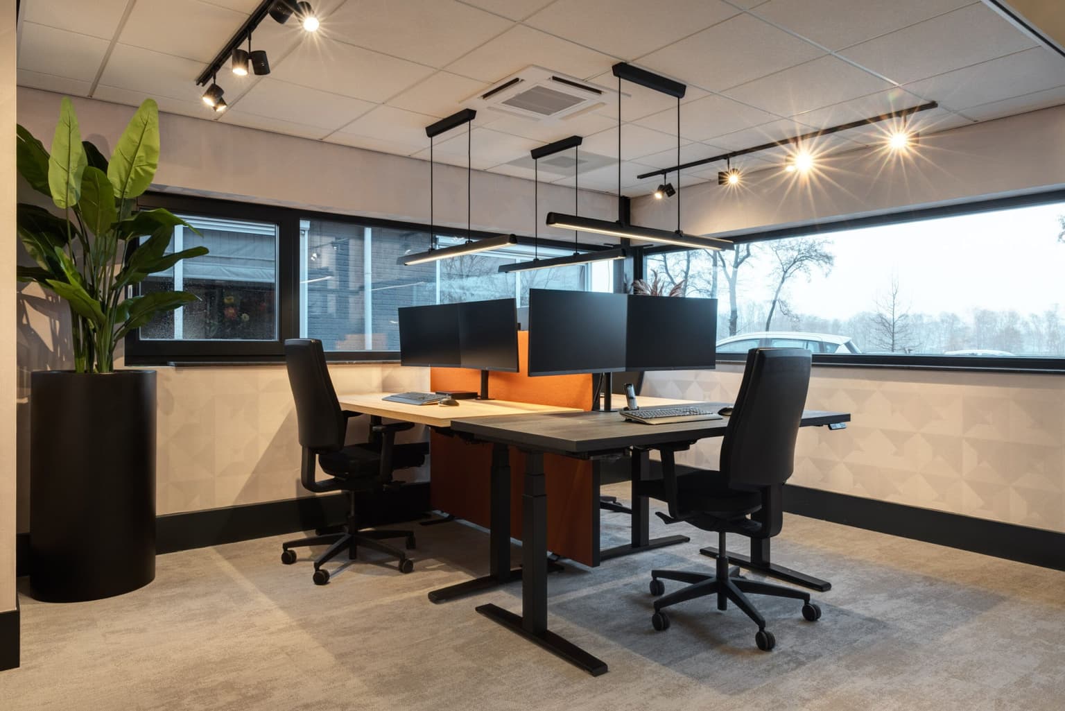 Werkplek met drie bureaus, bureaustoelen en een oranje akoestisch paneel.