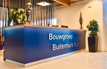 Blauwe balie met daarop het logo van Bouwgroep Buitenhuis, achter de balie staat een wandmet stokken en planten.