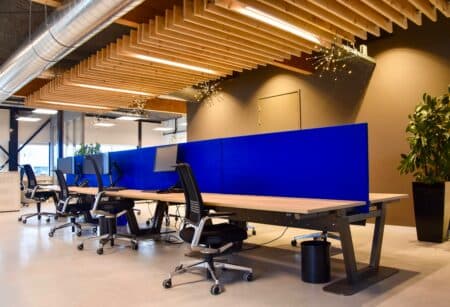 Ruimte met verschillende werkplekken naast en tegenover elkaar met een kobaltblauwe akoestische scheidingswand ertussen.