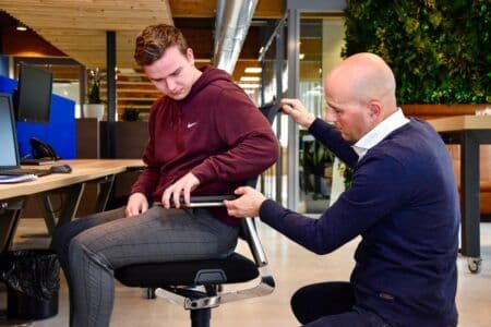 Jongen met een bordeauxrode hoodie zit op een stoel terwijl iemand anders de functies uitlegt.