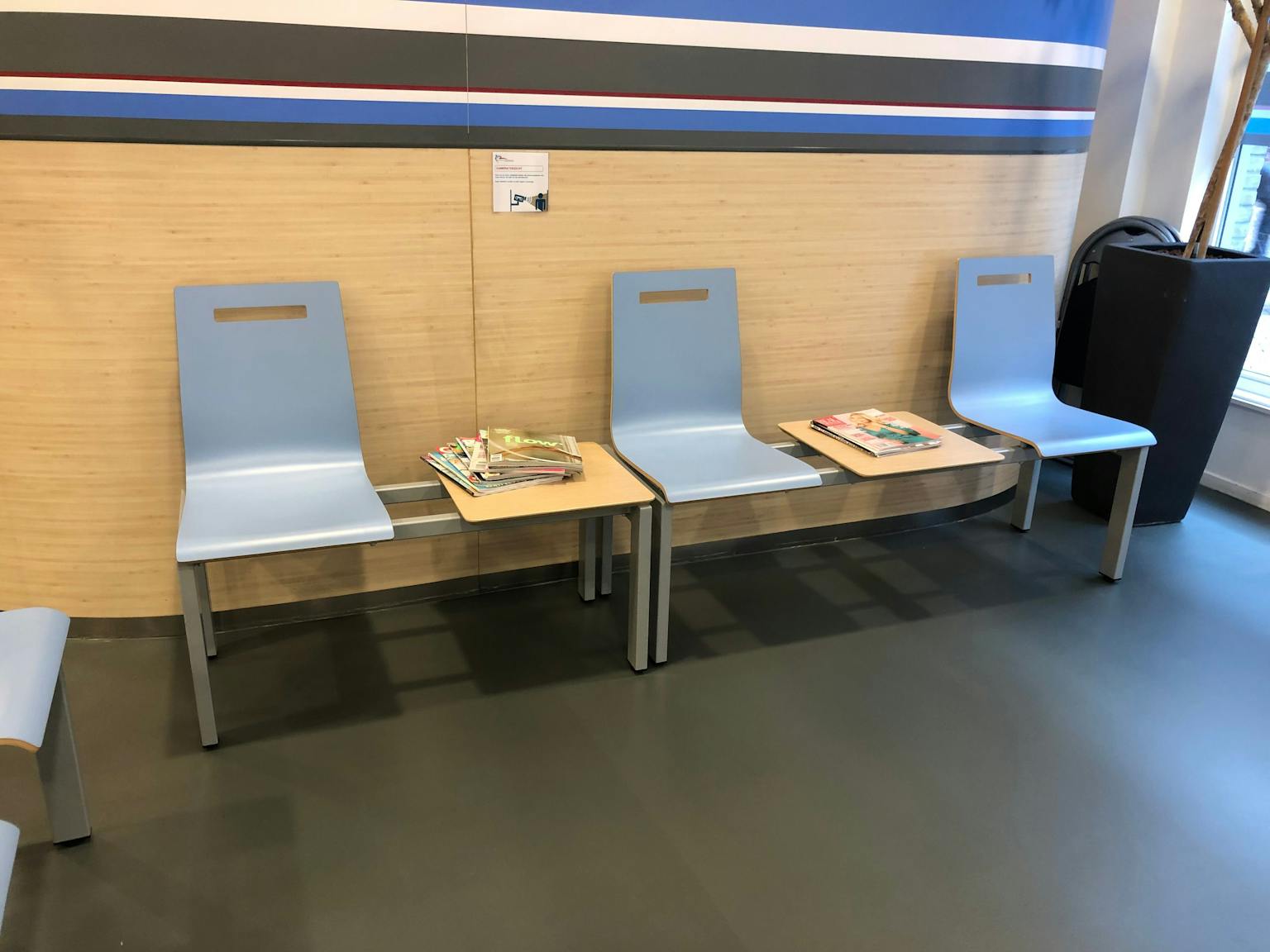 Wachtkamer met daarin blauwe stoelen en tussen de stoelen in een tafel met daarop tijdschriften.