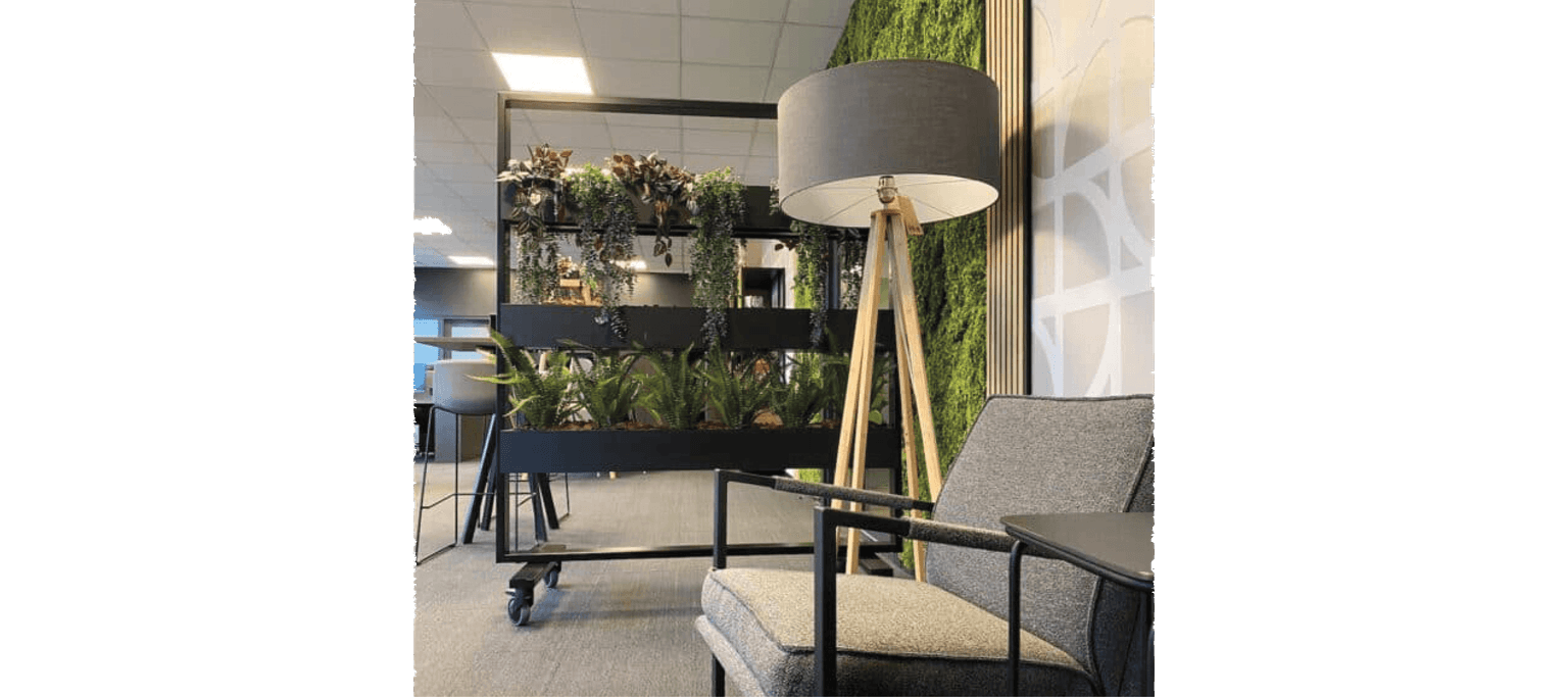 Zithoek in een kantooromgeving. In de voorgrond staat een grijze stoel. Daaracher een lamp. En daarachter een zwarte, verrijdbare plantenbak en roomdivider.